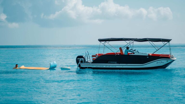 Aerial top-down view of the 28 ft bowrider La Otra anchored in crystal-clear turquoise water near Cancun, bold black hull with vibrant orange-red leather seating and Mercury outboard