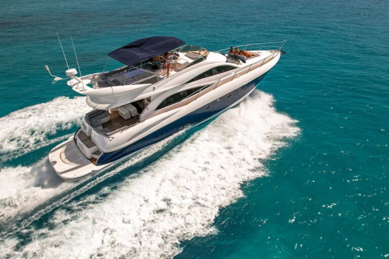 Aerial bow view of the 60 ft Sunseeker yacht charter at anchor in crystal-clear turquoise water, two women sunbathing on the bow sun pad with guests on upper deck at Riviera Maya