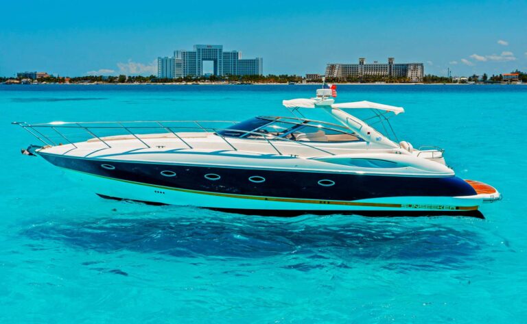 Starboard profile of 46 ft Sunseeker Agavero luxury yacht charter at anchor in crystal turquoise Caribbean water, dark blue hull with gold stripe and Cancun resort skyline behind