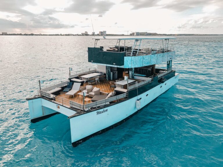 Aerial stern view of 60 ft Hasten party motor boat with two-story design, teak main deck lounge, and turquoise Caribbean water off Cancun