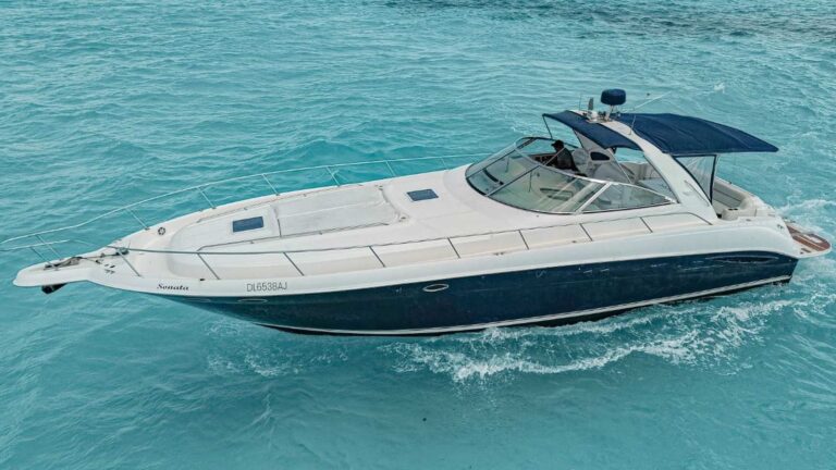 Aerial side of 47 ft Sea Ray Sonata navy-hull yacht with blue bimini, anchored on turquoise Caribbean water for a Cancun luxury yacht charter rental.
